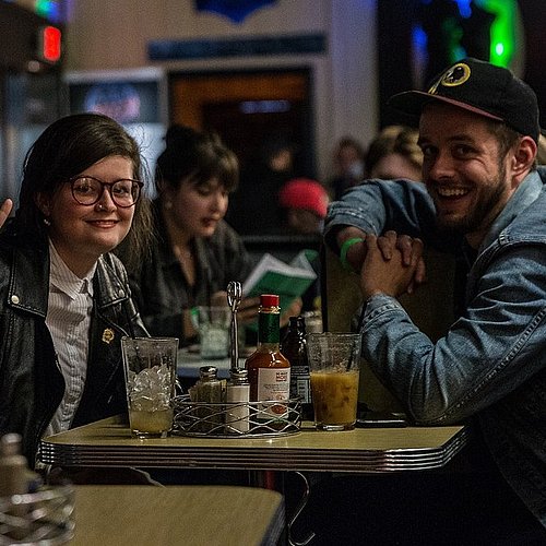 Junge leute sitzen mit Getränken in einer Bar und lachen in die Kamera