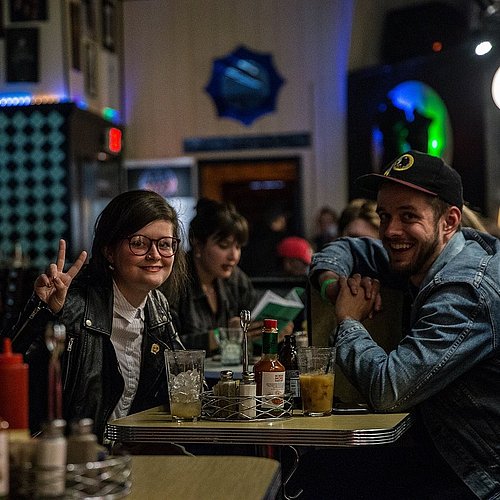 Junge leute sitzen mit Getränken in einer Bar und lachen in die Kamera