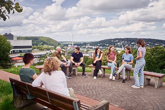 Personen sitzen auf Bänken auf dem Flügelhügel und man sieht im Hintergrund die Sicht ins Tal