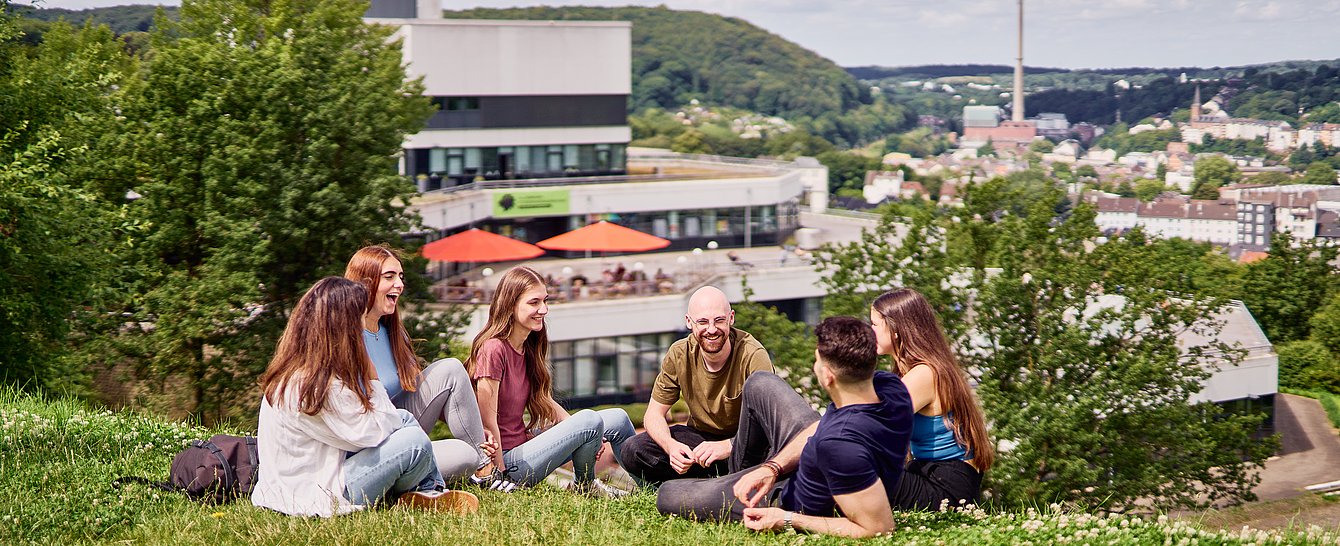 Gruppe von jungen Menschen sitzt auf einer Wiese vor der Mensa der Universität