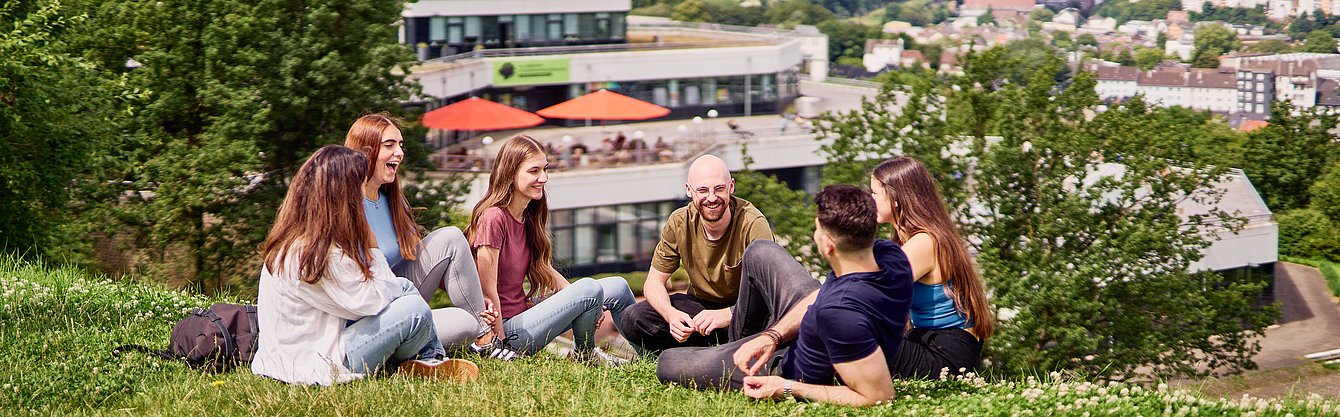 Gruppe von jungen Menschen sitzt auf einer Wiese vor der Mensa der Universität